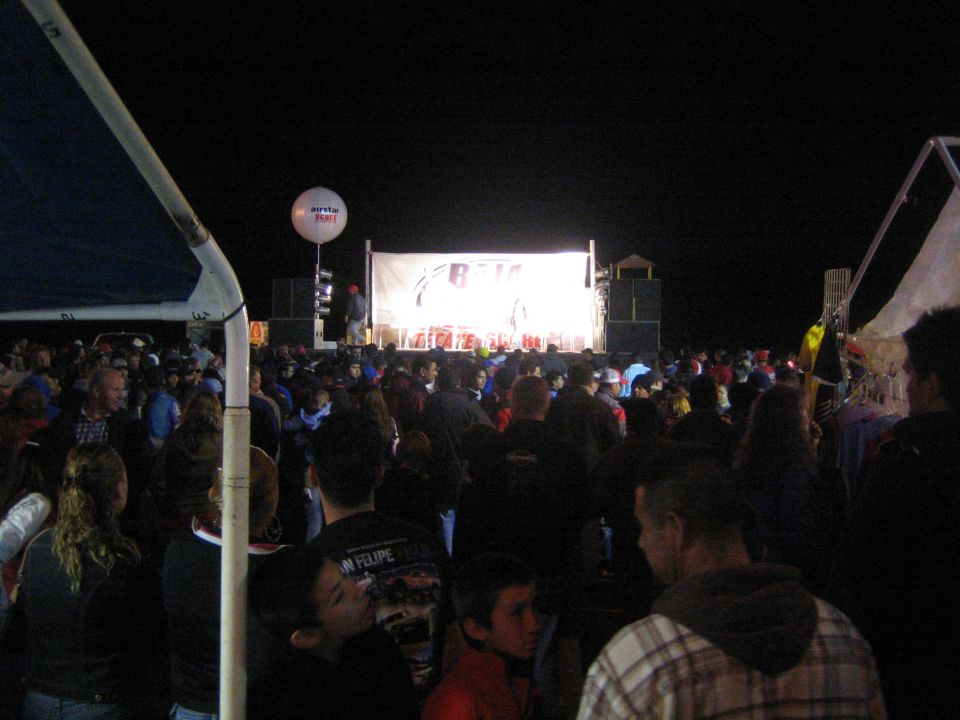 Crowd facing a lit Baja-branded stage under a tent at a night event