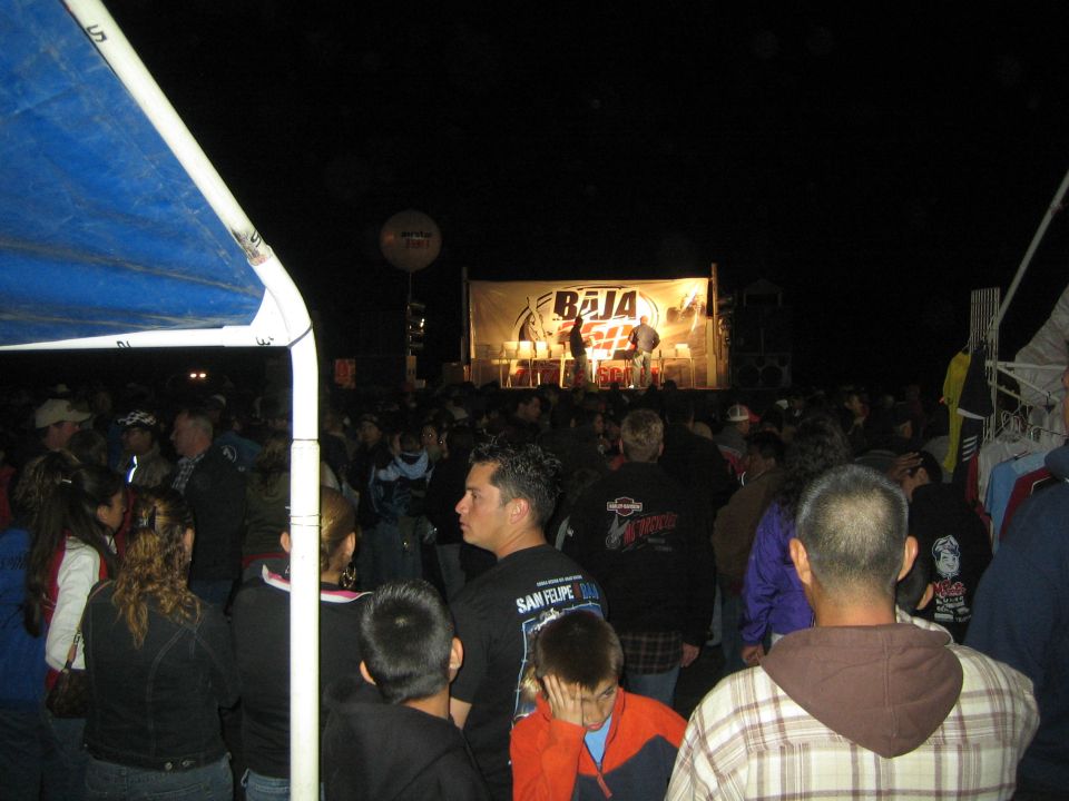 Spectators watching a Baja 250 stage event at night from under a tent