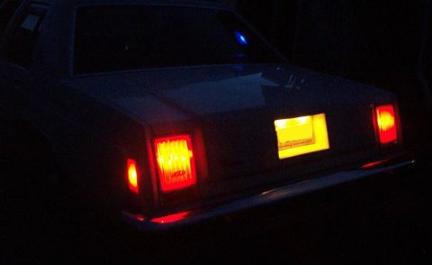 1985 Ford LTD Crown Victoria - The rear of a 1985 Ford Crown Victoria LTD is visible at night, with its taillights and license plate light illuminated.