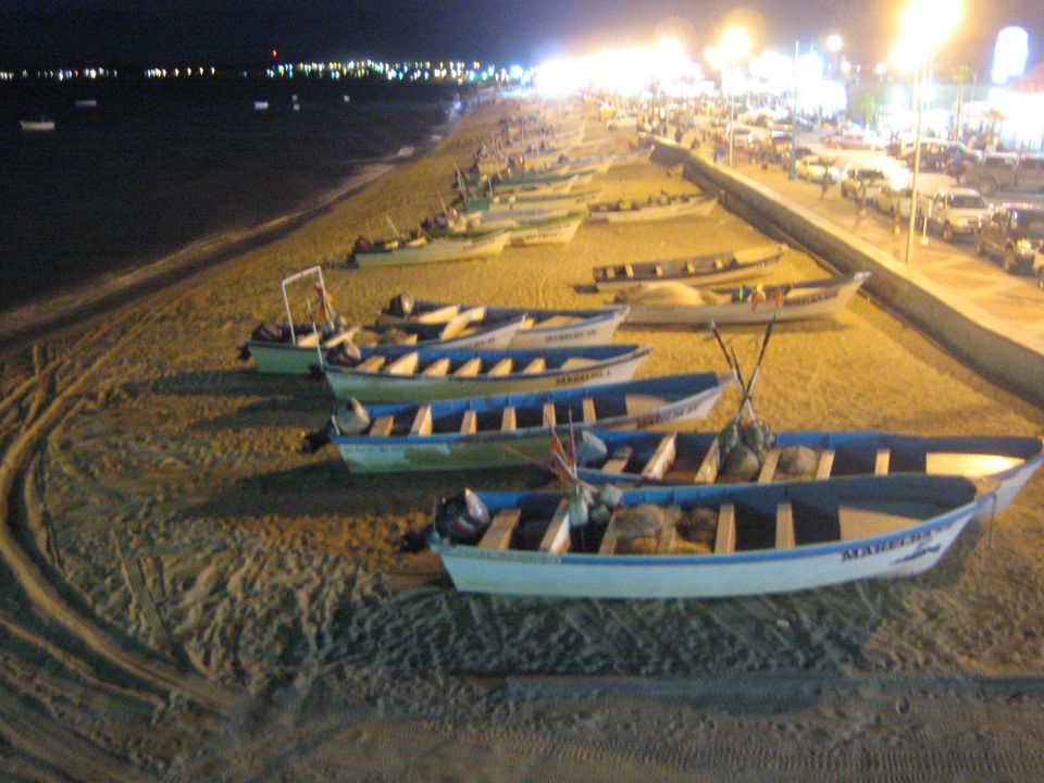 Rows of small fishing pangas beached on sand at night with city lights in the background