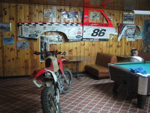Red dirt bike in a wood-paneled bar beside a pool table and a signed Baldwin 86 race panel