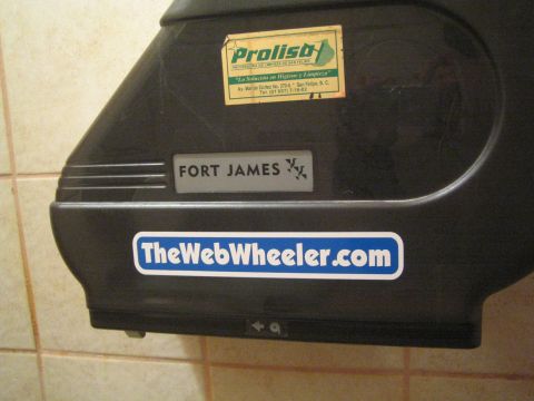 Wall-mounted paper towel dispenser with Prolisa, Fort James and TheWebWheeler.com stickers in a tiled restroom