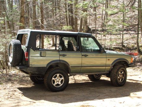 1996 Ford Bronco - This Land Rover Discovery is parked on a dirt path surrounded by trees in a wooded area.