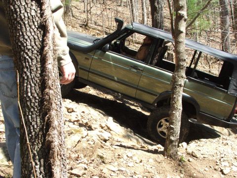 1996 Ford Bronco - A green SUV navigates a challenging, rocky off-road path with a driver inside.
