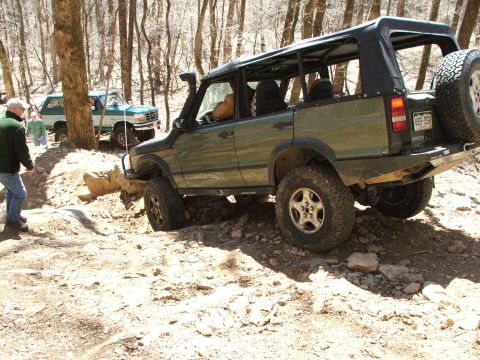 1996 Ford Bronco - A green off-road SUV navigates a rocky trail, with another vehicle in the background.