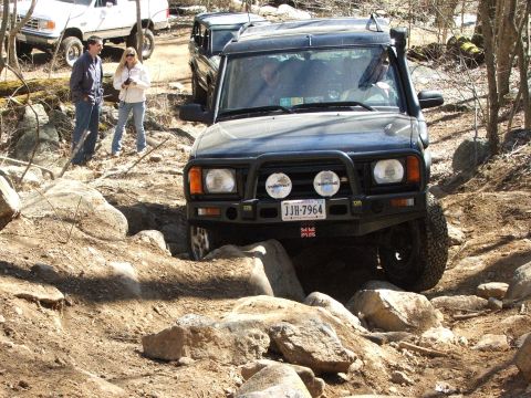 1996 Ford Bronco - A black SUV tackles a challenging off-road course with other vehicles and people nearby.