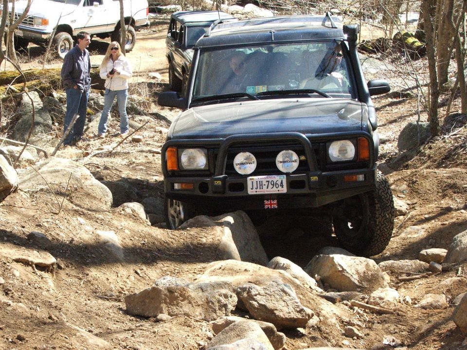 Black SUV with a snorkel and bull bar navigating a rocky trail. License plate JJB-7964 is visible