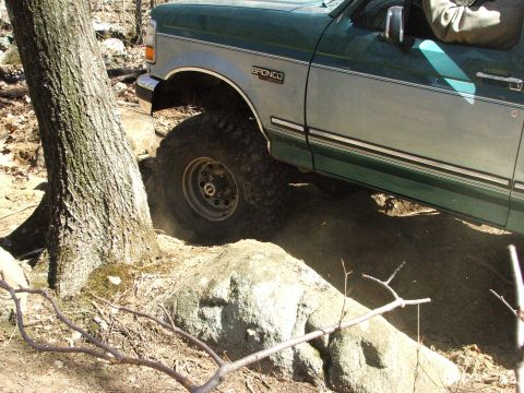 1996 Ford Bronco - A 1996 Ford Bronco maneuvers through a challenging off-road course with large rocks and trees.