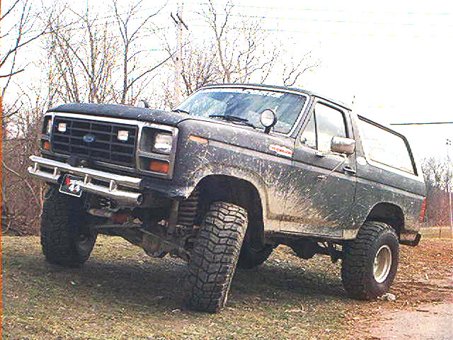 Mud-splattered Ford Bronco lifted with large tires, parked on uneven ground