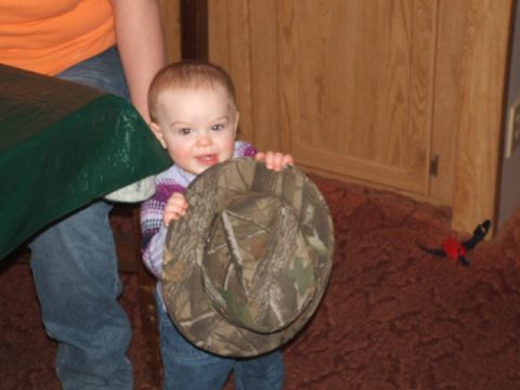 1966 Ford Ranchero - A baby smiles while holding a camouflage hat, with a green table to the left and wooden paneling in the background.