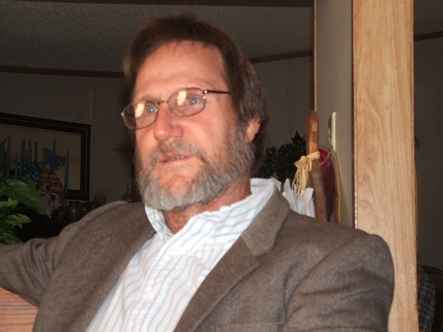 Man with glasses and beard wearing a brown jacket over a striped shirt