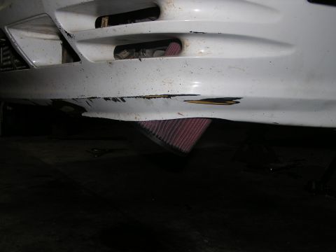 1993 Ford Taurus - Close-up of a damaged white car bumper revealing an aftermarket air intake system.