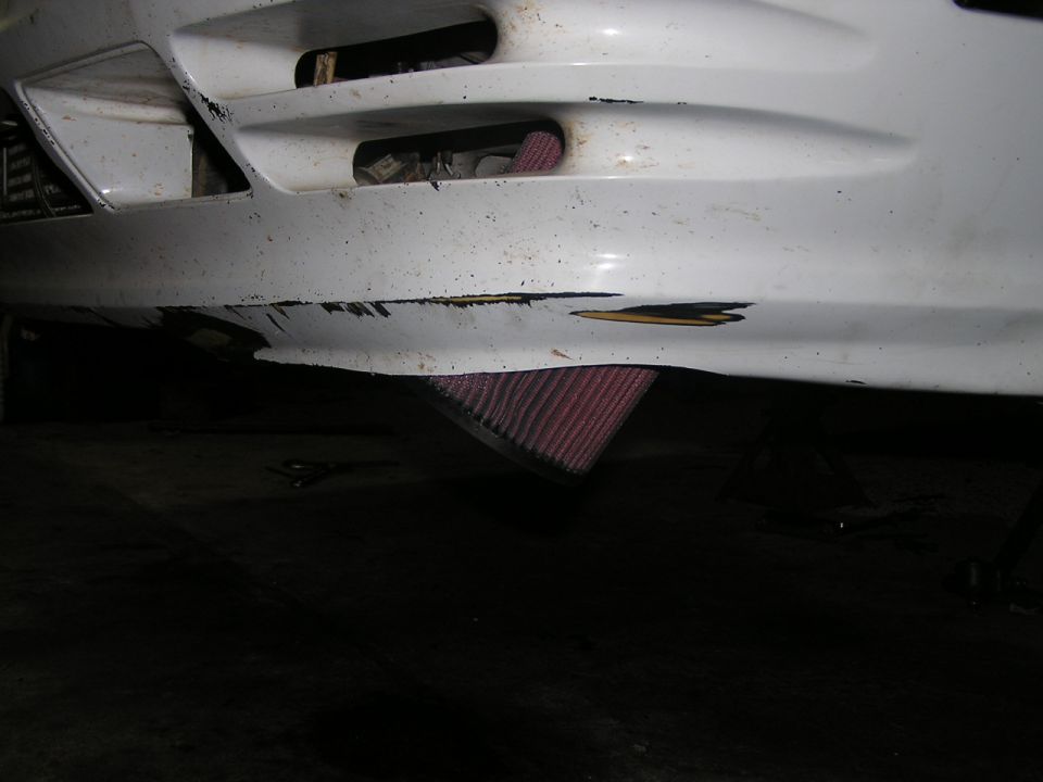 White car bumper with visible damage and an exposed red cone air filter underneath