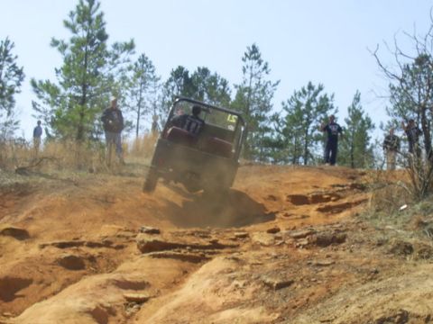 1995 Ford Bronco - Open-bodied flat-fender trail buggy with a roll bar and red bench seat cresting a red-clay ledge, one front wheel lifted off the ground as…