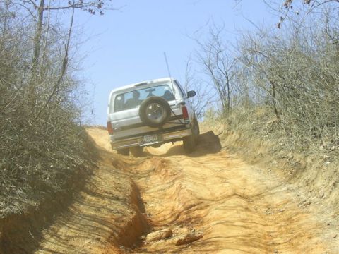 1995 Ford Bronco - White full-size Ford Bronco seen from directly behind as it crests a steep, deeply rutted red-clay hill climb lined with bare winter brush.…