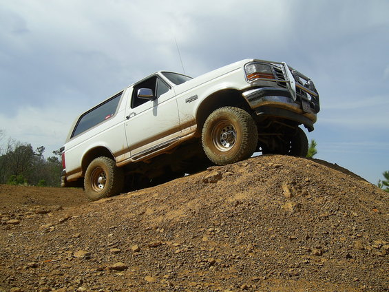 White Ford Bronco with brush guard climbing a red dirt mound, low 3/4 front angle