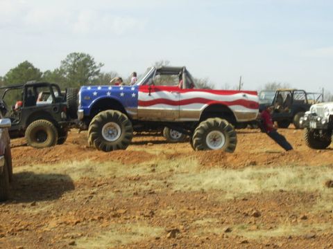 1995 Ford Bronco - Side view of a topless lifted 4x4 painted in a full American-flag scheme, stars on the front fender and red-and-white stripes down the body…