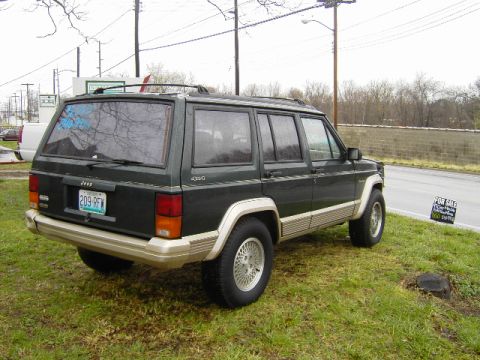 1993 Jeep Cherokee - Rear view of a 1993 Jeep Cherokee parked on a grassy area next to a road.
