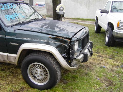 1993 Jeep Cherokee - A damaged 1993 Jeep Cherokee is parked next to a white pickup truck in an outdoor lot.