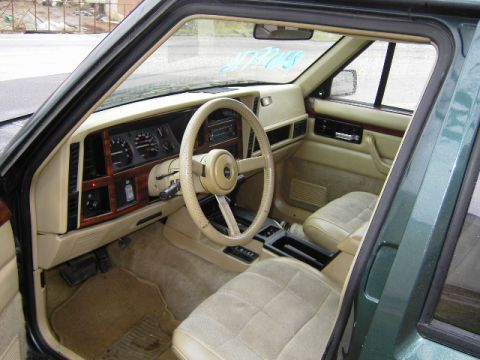 1993 Jeep Cherokee - The interior of a 1993 Jeep Cherokee features a tan dashboard, steering wheel, and cloth seats.