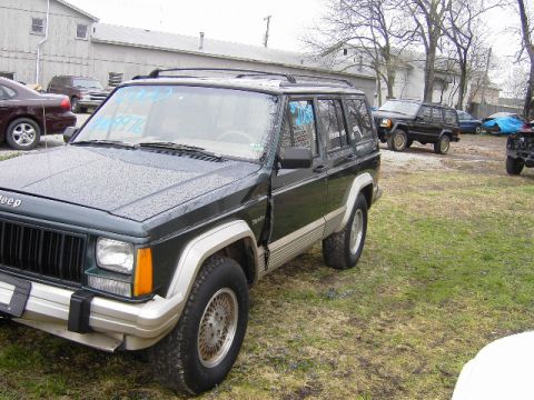 1993 Jeep Cherokee - A dark green Jeep Cherokee is parked in a lot with other vehicles visible in the background.