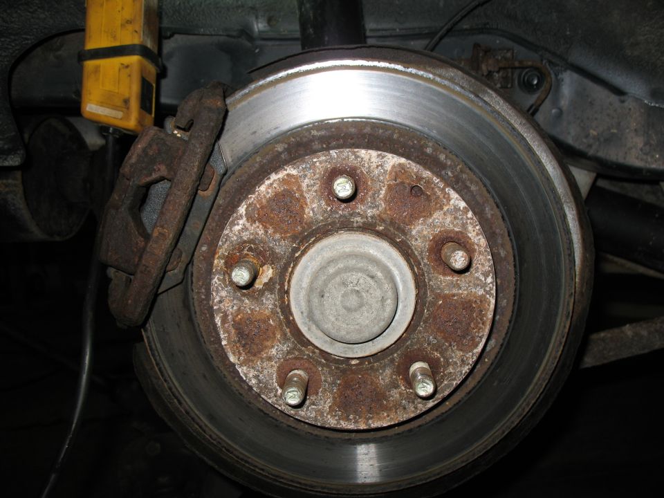 Close-up of a rusty brake rotor and caliper assembly on a vehicle's rear axle