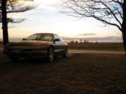 1996 Ford Probe - A 1996 Ford Probe is parked on a grassy area with trees and a rural landscape in the background during sunset.