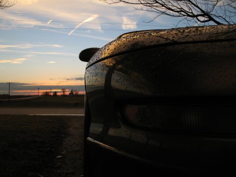 1996 Ford Probe - The back of a car is visible against a sunset sky with clouds and distant farm buildings.