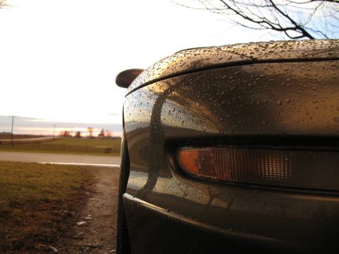 1996 Ford Probe - A car's front corner is covered in water droplets, with a rural landscape in the background.