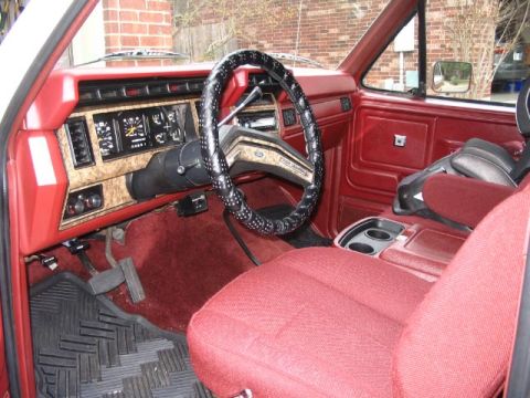 1986 Ford Bronco - The interior of the vehicle shows red upholstery on the seats and dashboard, with a black steering wheel and a functional center console.