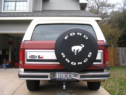 1986 Ford Bronco - The rear of a red Ford Bronco shows a spare tire cover with the model name and a horse emblem.