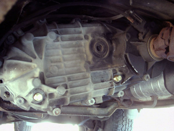 Underside view of an aluminum transfer case with driveshaft and exhaust alongside