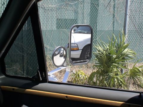 1993 Ford C-350 (Centurion Conversions) - Towing mirror reflects a white pickup truck, with a fence and palm plants in the background.