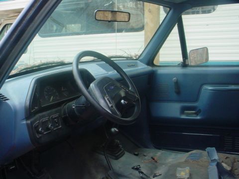 1988 Ford Bronco - The interior of a vehicle shows a blue dashboard, steering wheel, and manual transmission shifter.