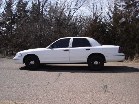 2000 Ford Crown Victoria - A white 2000 Ford Crown Victoria is shown from the side, parked on a road with trees in the background.