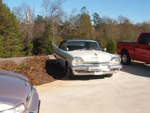 1966 Ford Ranchero - A white convertible with distinctive tail fins is parked in a driveway next to a red pickup truck.