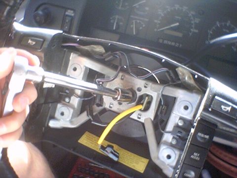 1994 Ford Bronco - Mechanic uses a socket wrench on the steering column assembly of a 1994 Ford Bronco, with a yellow wire and part of the dashboard visible.