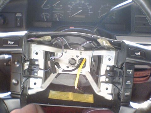 1994 Ford Bronco - Disassembled steering column reveals the clock spring and associated wiring, with dashboard gauges in the background.