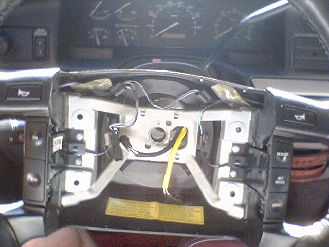 Steering column disassembled, showing clock spring mechanism and wiring. Dashboard gauges visible