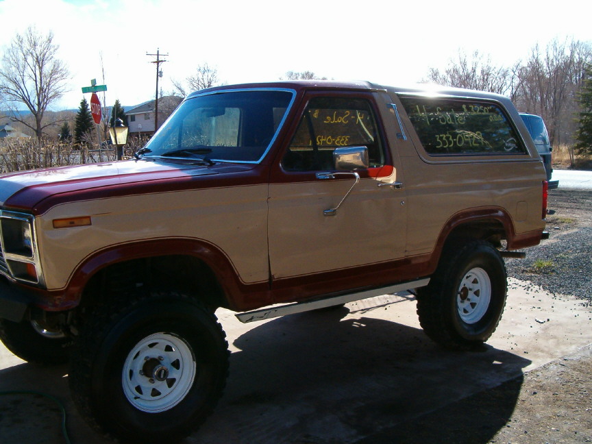 1985 Ford Bronco, tan and maroon two-tone paint, lifted with large tires. "For Sale" and phone number written on windows