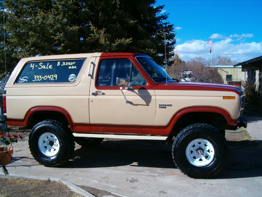 Tan and red 1980s full-size Ford Bronco for sale, lifted on white wheels