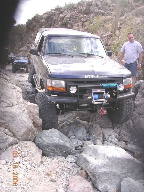 1994 Ford Bronco - A blue 1994 Ford Bronco tackles a challenging rocky off-road path, with another vehicle visible in the background.