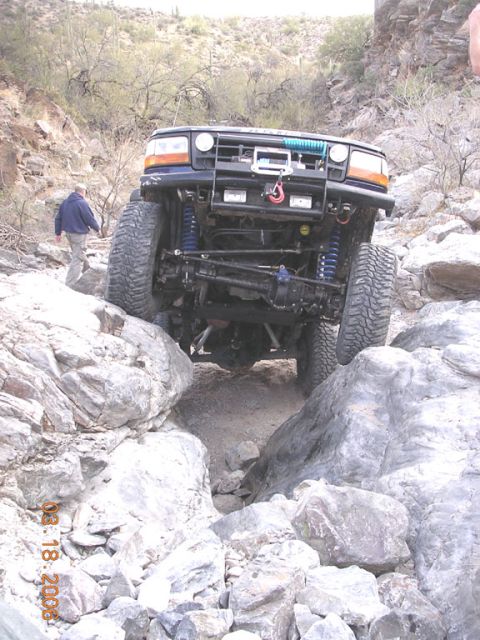 1994 Ford Bronco - This modified Ford Bronco is shown off-roading through a rocky terrain, with a person walking behind it.