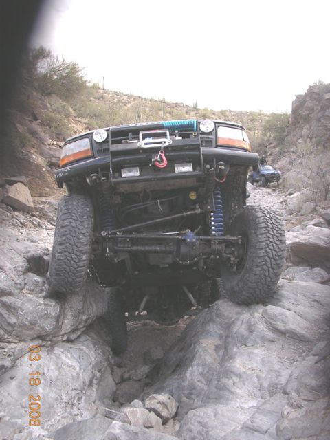 1994 Ford Bronco - A black Ford Bronco is shown off-roading on a rocky terrain, with another vehicle visible in the background.