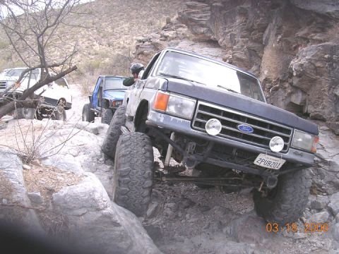 1994 Ford Bronco - This Ford Bronco is tackling a challenging off-road trail with other vehicles present.