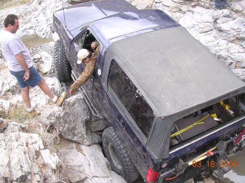 1994 Ford Bronco - A blue SUV is being carefully maneuvered over large rocks by its driver.