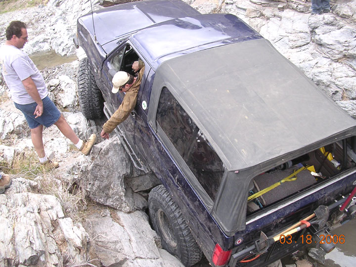 Dark blue Ford Bronco with soft top crawling over rocks off-road