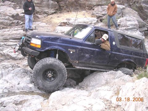 1994 Ford Bronco - A blue 1994 Ford Bronco is shown off-roading over large rocks.