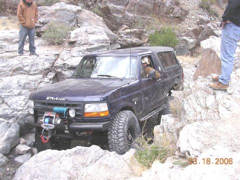 1994 Ford Bronco - A 1994 Ford Bronco is shown off-roading on a rocky terrain with two observers present.