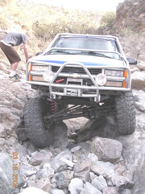 1994 Ford Bronco - A modified truck navigates a challenging rocky path, with a person observing.